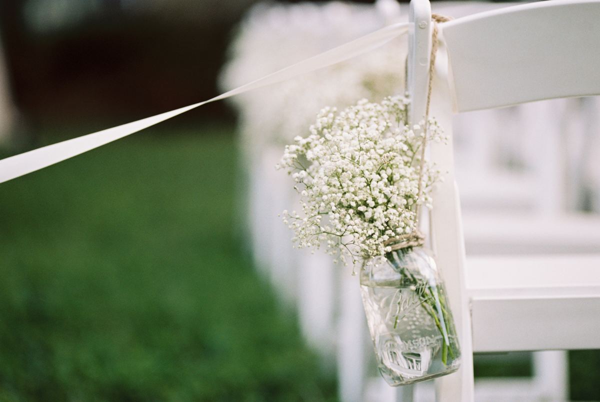 Baby&rsquo;s breath in a jar on a chair along a wedding aisle