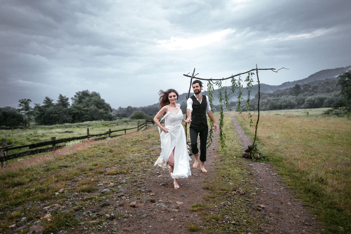 A newly married couple running hand in hand down a country lane