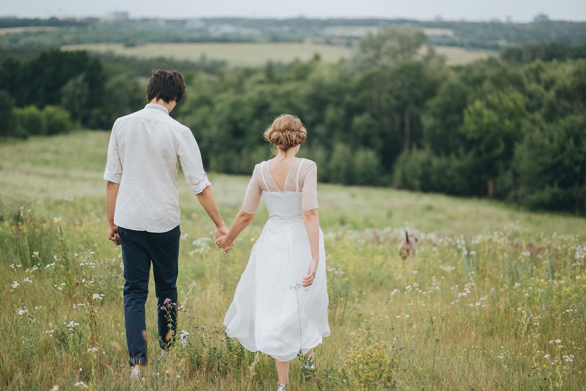 A couple walking hand in hand through a summer meadow